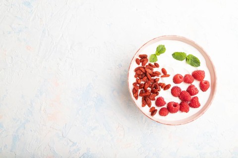 Yogurt with raspberry and goji berries in ceramic bowl on white concrete background. top view, flat