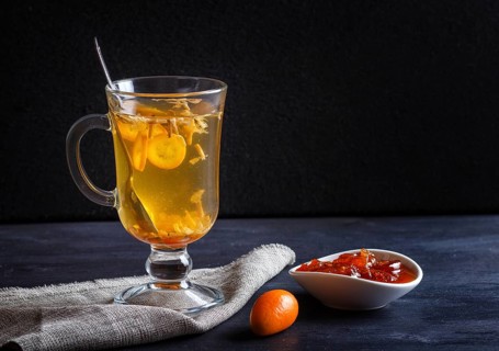 Jasmine tea with kumquat in a glass cup on a wooden board on a black background. close up, copy