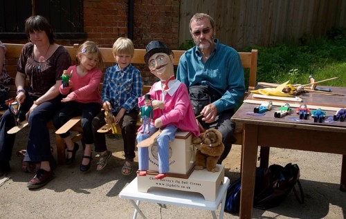 Man operating a traditional wooden jig doll dancer during a country folk event at Shottisham,