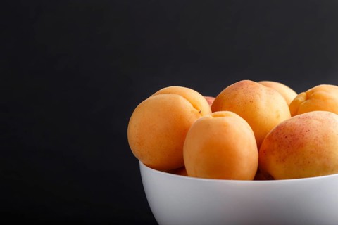 Fresh orange apricots in white bowl on black background. side view, close up, selective focus