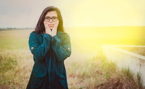 Portrait of beautiful woman with glasses in the field. Cute Girl in glasses with hands on cheeks