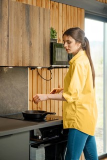 Young woman frying vegetables in a pan in the kitchen using electric stove