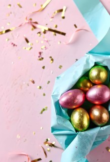 Small chocolate Easter eggs wrapped in shiny foil, placed on a bed of shredded pastel-colored