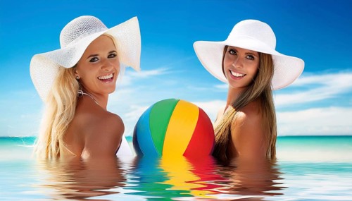 Two young woman in sun hats playing with a beach ball on the beach in the Caribbean