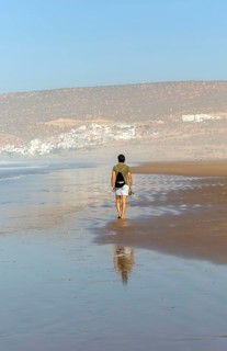 Man walking barefoot on sandy beach at low tide near village of Taghazout, Morocco, North Africa,