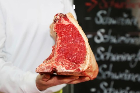 Butcher holds a dry aged T-bone steak in his hand