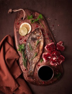 Fried dorado fish, with spices and herbs, on a wooden board, pomegranate sauce, close-up, no people