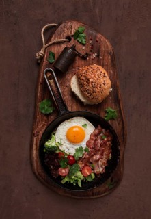 Fried egg, with bacon and vegetables, in a cast-iron frying pan, top view, homemade breakfast