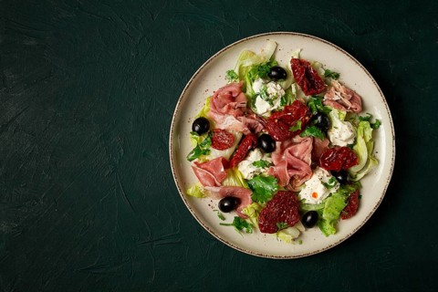 Salad with dried tomatoes, prosciutto, soft cheese, olives, homemade, top view