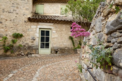 Natural stone wall with a red spur flower (Centranthus ruber) and old house with a door and roof in