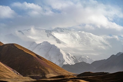 Dramatic mountain landscape, mountain valley, behind glaciated and snow-covered mountain peak Pik