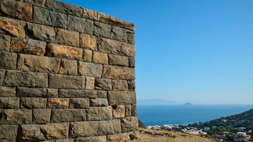 A massive stone structure overlooking the sea and the surrounding landscape under a clear sky,