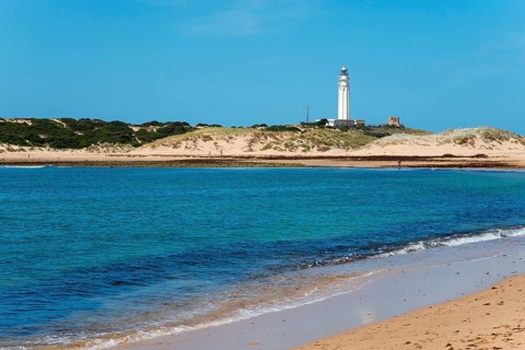 Sandy beach beach with lighthouse in the background, clear blue sea and bright dunes, Faro de