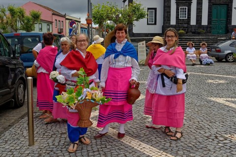 Women in colourful traditional dress stand on a street and smile, Fenais da Luz, Sao Miguel Island,