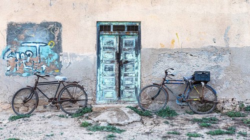 Old bicycles leaning against a house wall with an old wooden door, on the beach of Salalah, Dhofar