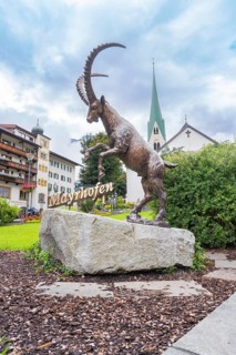 Bronze statue of a rising goat in front of a church and buildings in the background, Mayrhofen,
