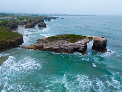 A striking rock in the shape of a natural bridge, surrounded by foaming waves and a tantalising