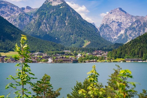 Lake surrounded by green mountains with a small cluster of houses in the sunlight, Achernsee,