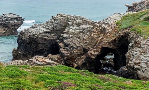 Rugged rock formations with natural arches and dense vegetation along the coast, Praia das