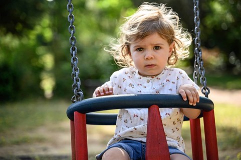 Child, 2 years, swings outdoors in a playground with a sunny atmosphere
