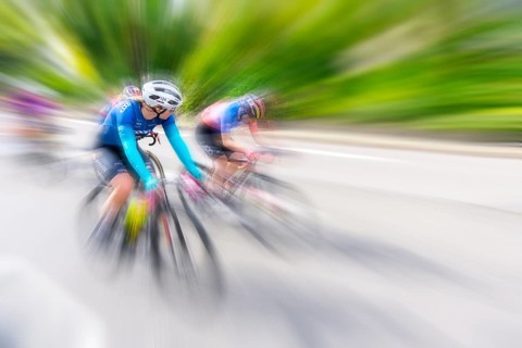 Two female cyclists in sportswear and helmets riding at high speed on a road, racing, the blur of