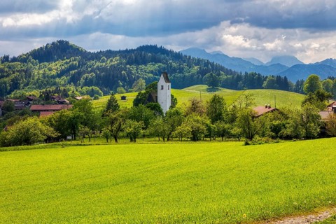 Rural scenery with church, green fields and hills under a cloudy sky, Steinkirchen