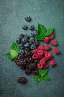 A mix of ripe berries, with leaves scattered on the table, raspberries, blackberries, blueberries,