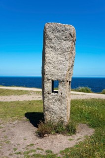 Single upright stone with square opening, in the background the sea and blue sky, Menhires por la