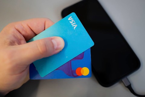 Hand holding two credit cards, for mobile payment, over a black smartphone on a grey background