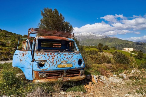 Abandoned rusty blue car on a green field with mountains in the background, wrecked vehicle, Crete,