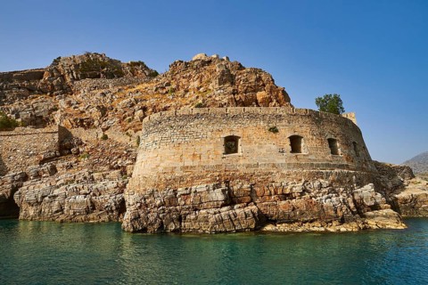Ruins of an ancient fortress on a coastal rock formation with clear sky and sea, Venetian sea