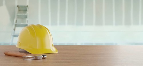 Yellow hard hat and hammer resting on a wood surface in front of drywall and ladder banner