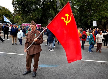 A man wears a Russian uniform and holds a flag of the former Soviet Union during the demonstration