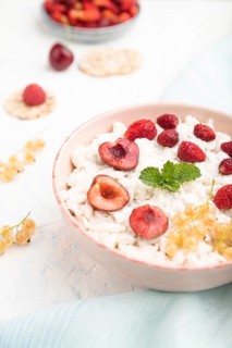 Rice flakes porridge with milk and strawberry in ceramic bowl on white concrete background and blue