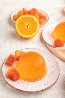 Papaya and orange jelly on gray concrete background and orange linen textile. side view, flat lay,