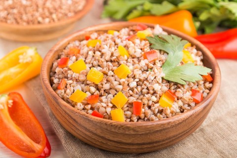 Buckwheat porridge with vegetables in wooden bowl on a white wooden background and linen textile.