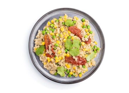 Quinoa porridge with green pea, corn and dried tomatoes on ceramic plate isolated on white