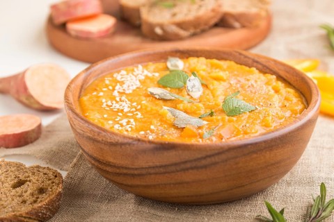 Sweet potato or batata cream soup with sesame seeds in a wooden bowl on a white wooden background