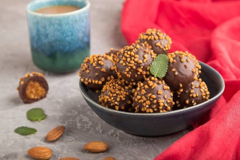 Chocolate caramel ball candies with almonds and a cup of coffee on a gray concrete background and