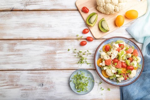 Vegetarian salad of cauliflower cabbage, kiwi, tomatoes, microgreen sprouts on white wooden