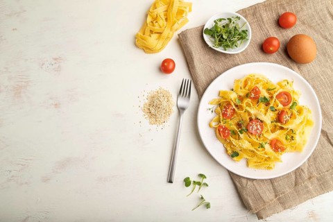 Reginelle semolina pasta with tomato, eggs, sesame and microgreen sprouts on a white wooden
