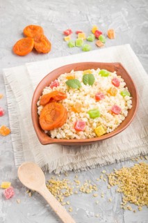 Bulgur porridge with dried apricots and candied fruits in clay bowl on a gray concrete background