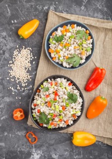 Pearl barley porridge with vegetables in blue ceramic bowls on a black concrete background and