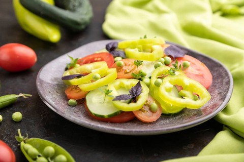 Vegetarian salad from green pea, tomatoes, pepper and basil on a black concrete background and