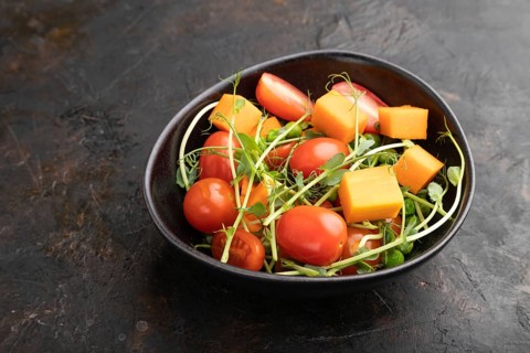 Vegetarian vegetable salad of tomatoes, pumpkin, microgreen pea sprouts on black concrete