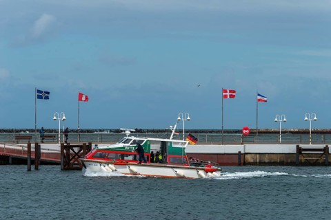 Dune ferry arrives in Heligoland harbour, flags in the wind, pier, offshore island of Heligoland,