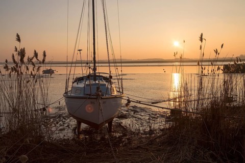 Yacht at moorings winter sunset, River Deben, Ramsholt, Suffolk, England, UK
