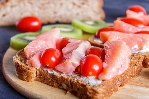 Smoked salmon sandwiches with butter and cherry tomatoes on black wooden background. close up