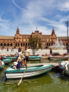 Tourists in rowing boats on a canal, pedestrians on Plaza de Espana, Plaza de España, Seville,