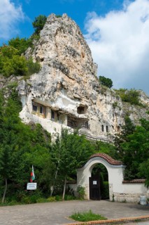 Monastery complex in a rocky landscape with green gate and flag, Bulgarian Orthodox cave monastery,